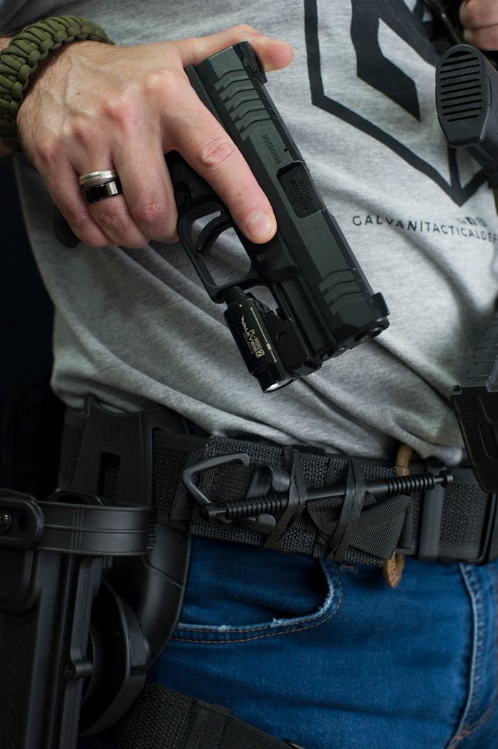 Detailed view of a person holding a pistol with a tactical belt showcasing holster and gear.
