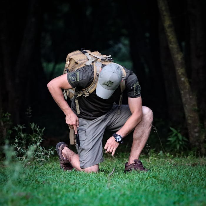 A man crouches in a forest, wearing a backpack and cap, perfect for adventure and hiking themes.