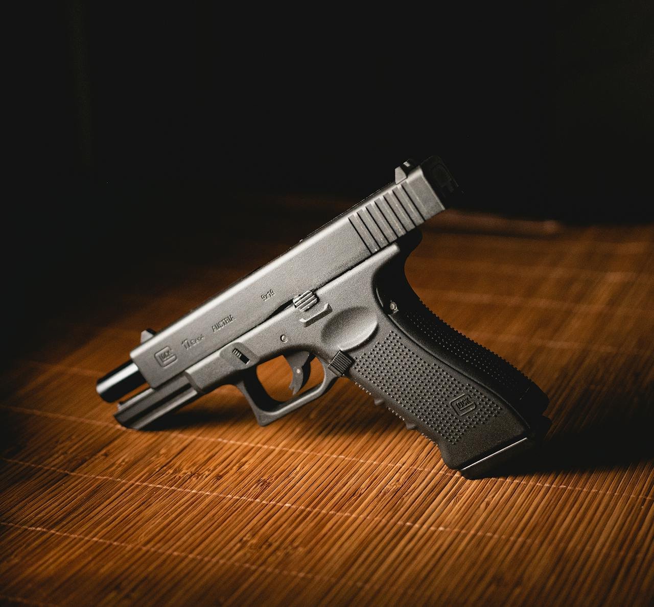 Close-up shot of a modern handgun placed on a bamboo mat, indoors.