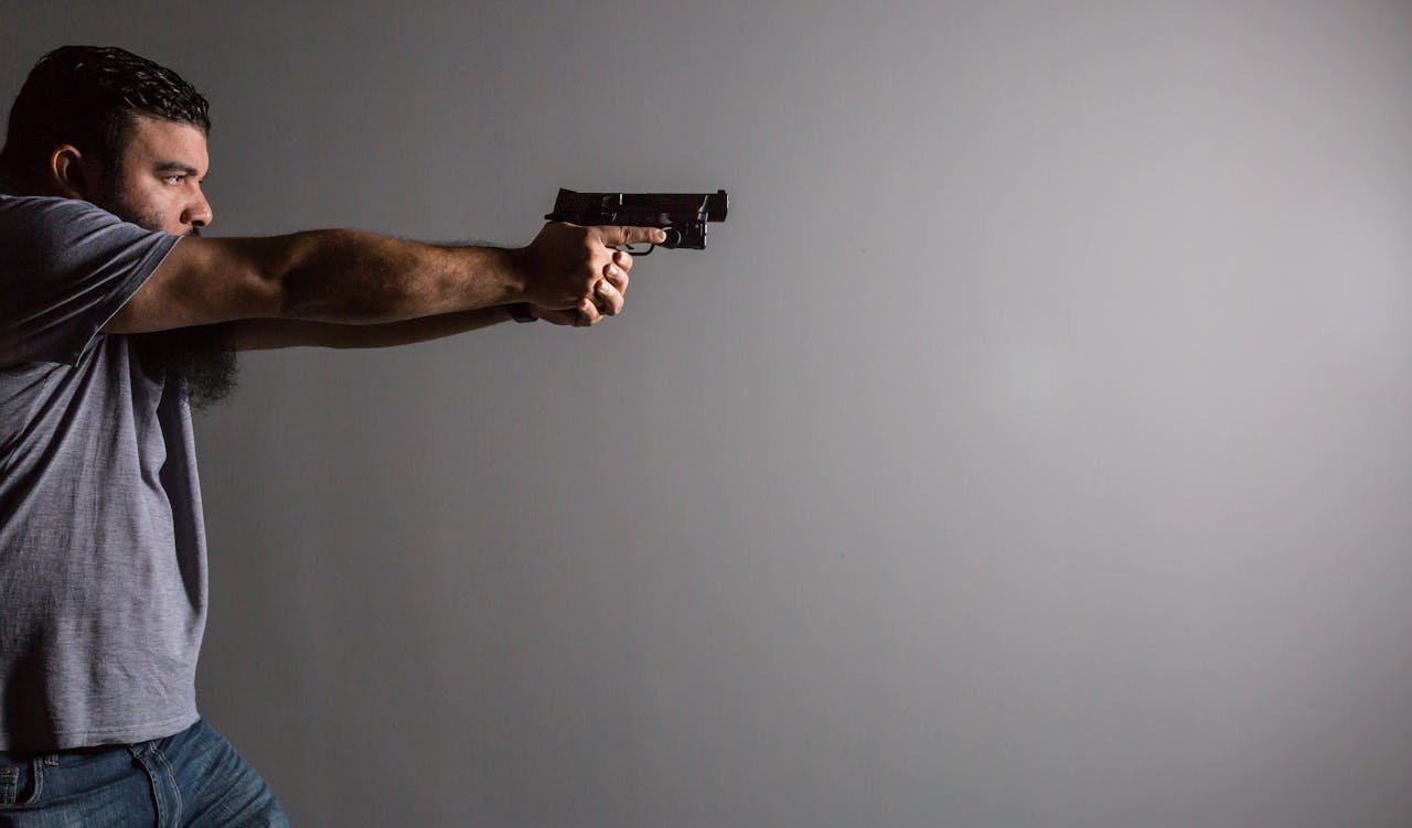 Man aiming a handgun indoors against a blank wall.